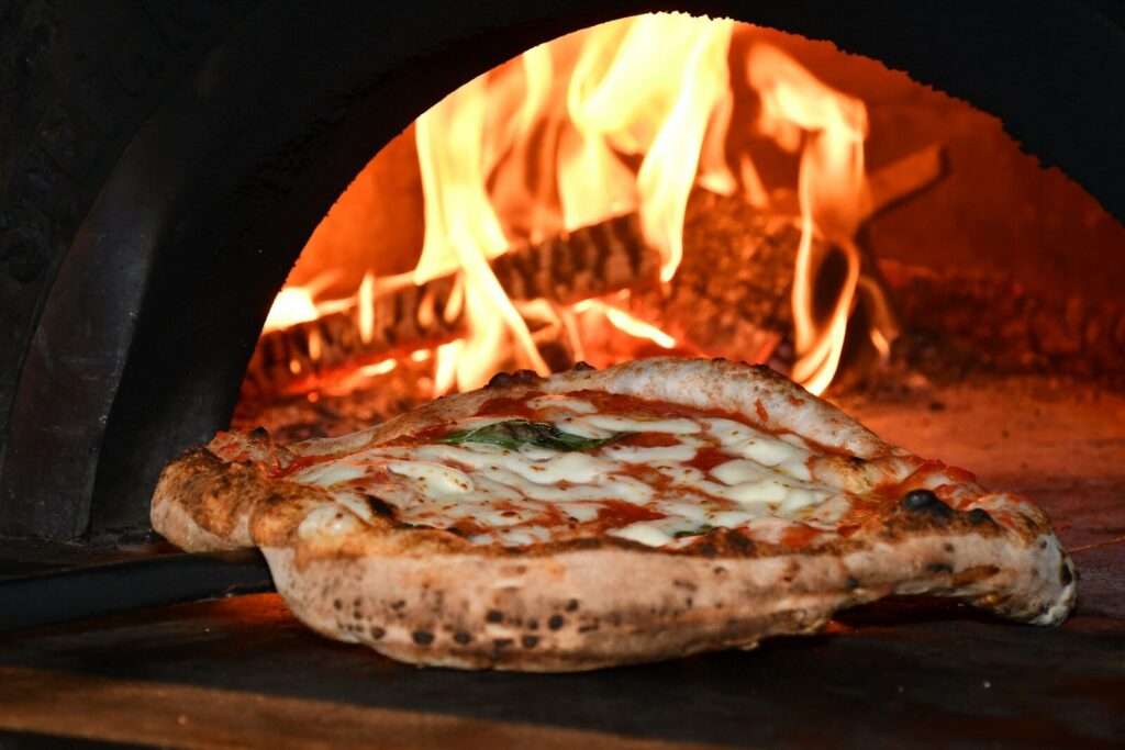 A pizza with melted cheese and tomato sauce baking in a wood-fired oven